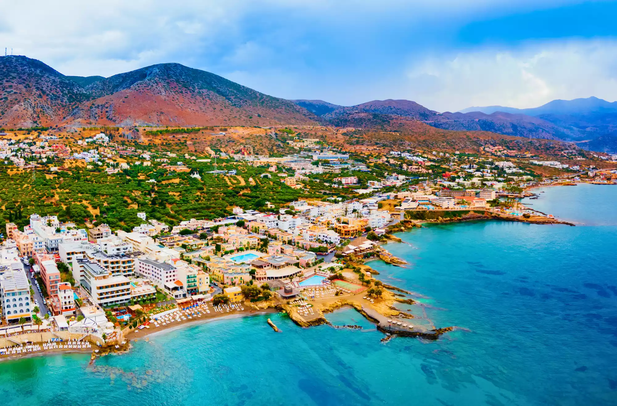 Hersonissos - in Grecia - vista dall'alto con le splendide spiagge bagnate da un mare cristallino e diverse strutture ricettive con piscina. Sullo sfondo le colline e una natura rigogliosa.