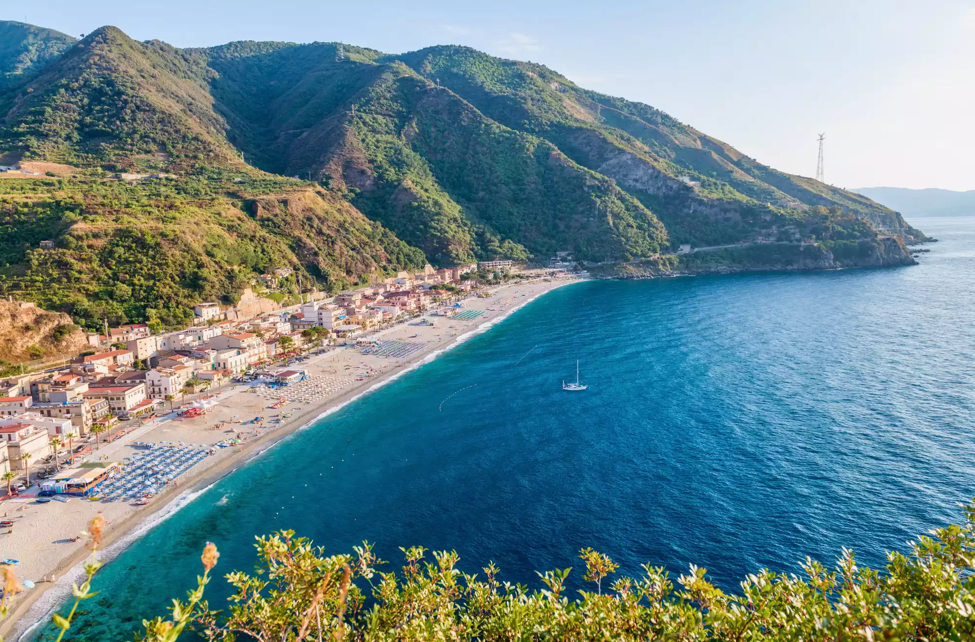 Veduta panoramica di Scilla in Calabria con la spiaggia di Marina Grande, le case colorate sul litorale e le colline verdi a picco sul mare Tirreno