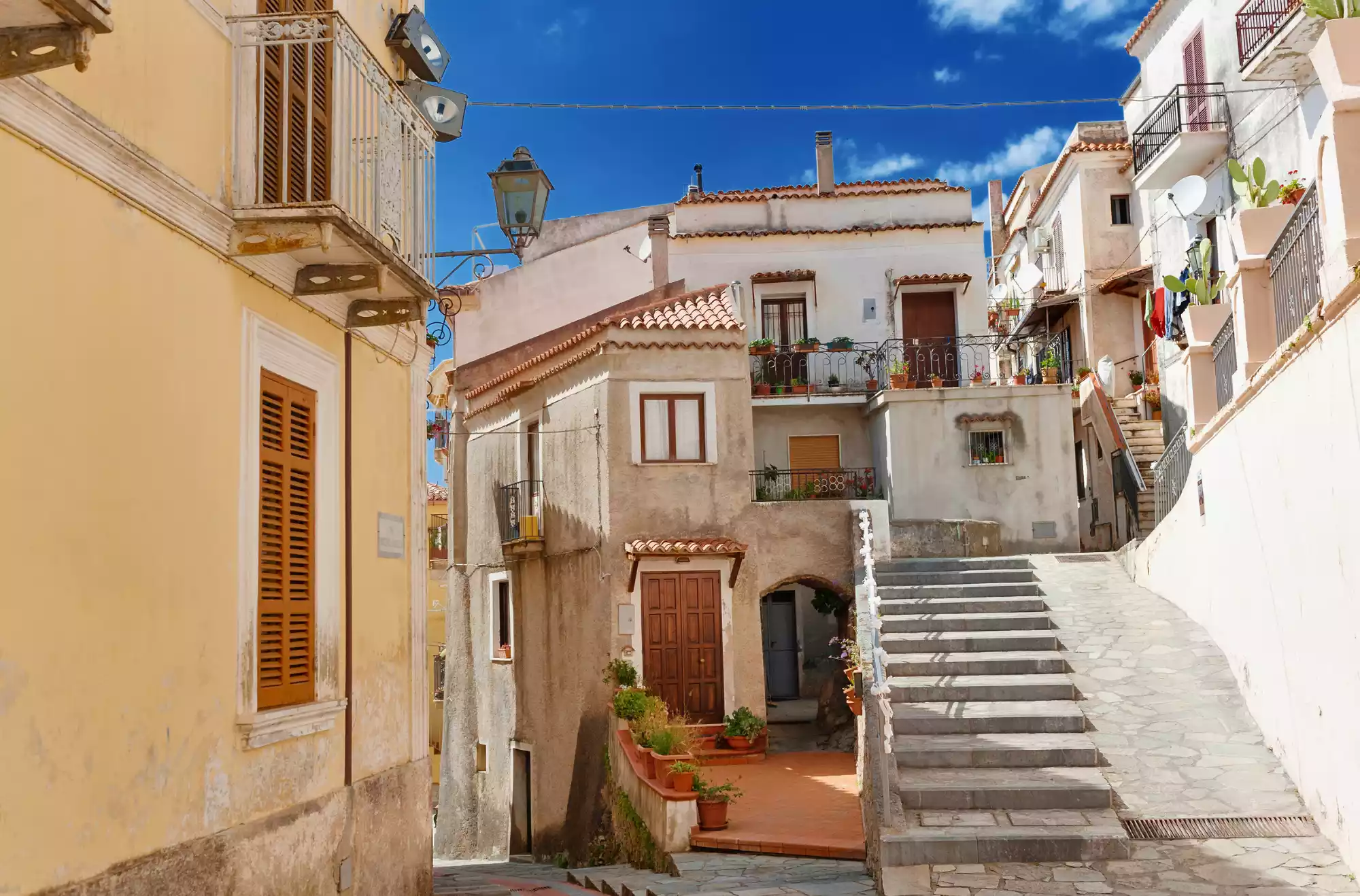 Scorcio del centro storico di San Nicola Arcella con case in pietra, scale in salita e balconi fioriti sotto un cielo azzurro