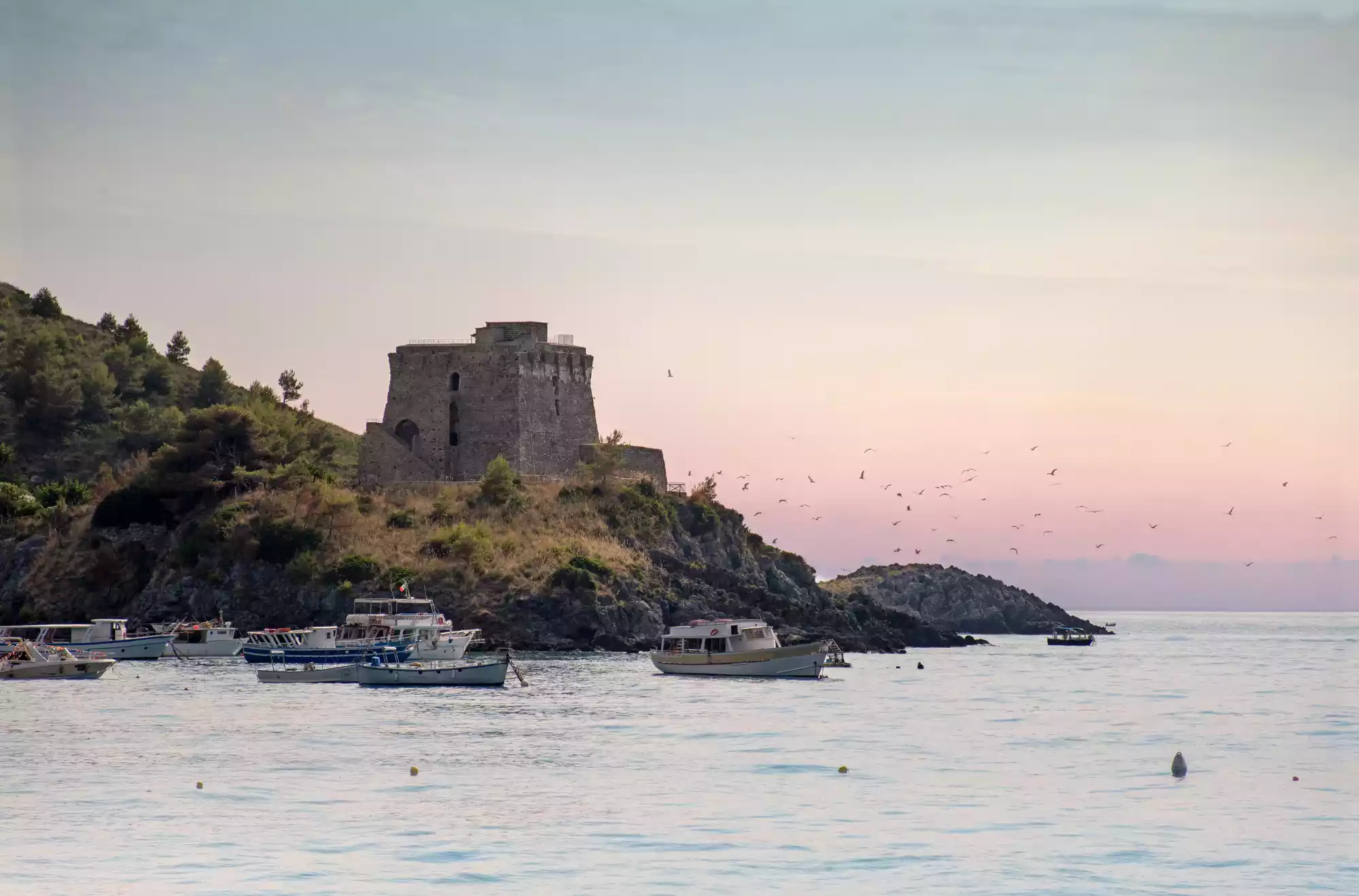 Torre di Crawford a San Nicola Arcella al tramonto, vista dalla baia con barche ormeggiate e cielo rosa pastello