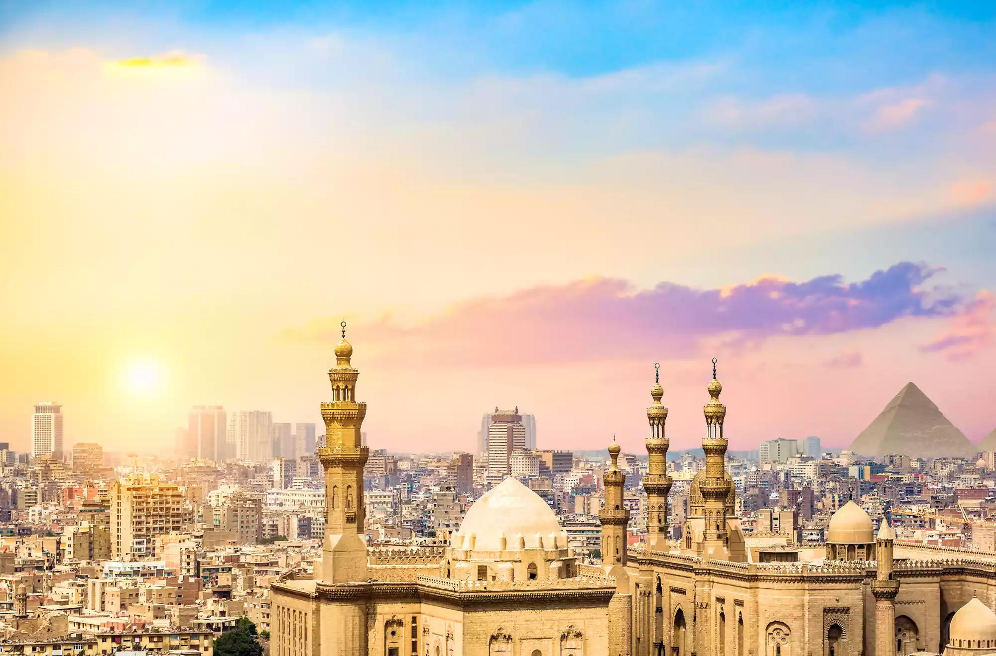 Panorama del Cairo al tramonto con moschee e in lontananza una piramide di Giza.